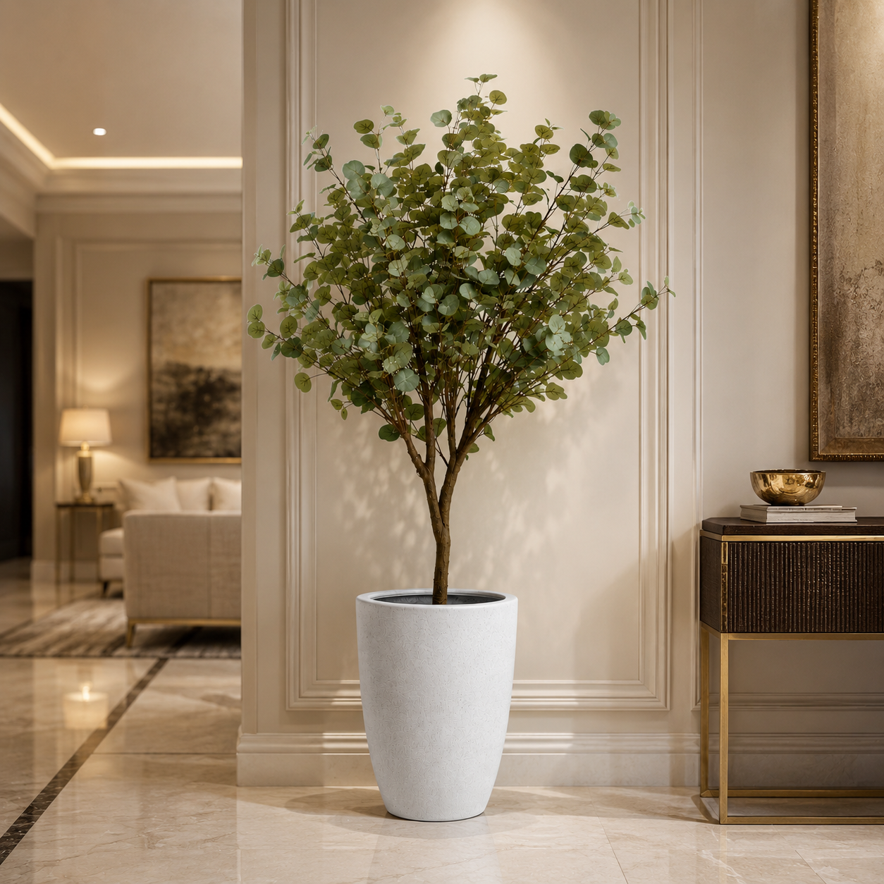 A potted artificial eucalyptus tree with green leaves and a brown trunk, displayed in a tall white cylindrical planter on a polished marble floor inside a luxurious, elegant interior hallway.
